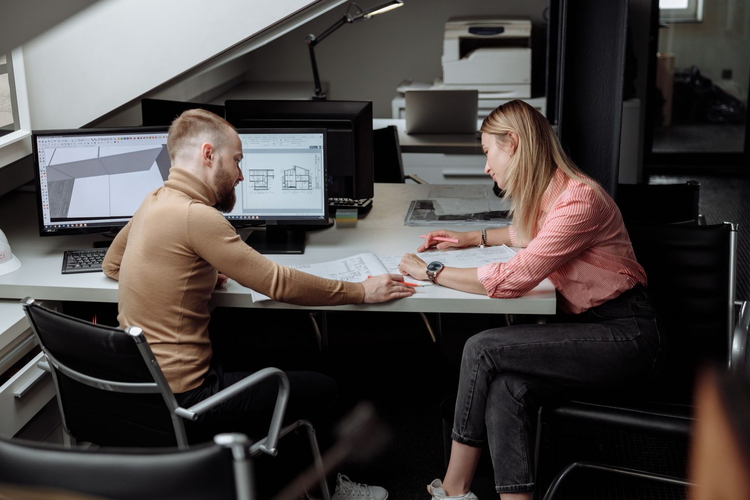 Twee mensen overleggen aan een werkplek met CAD-tekeningen op de schermen