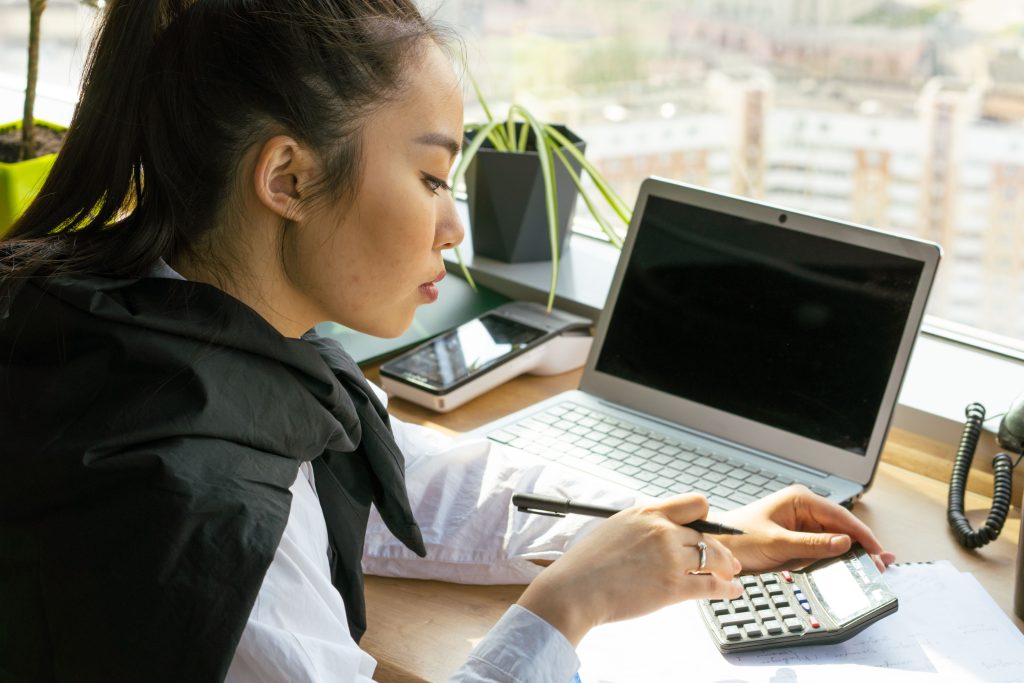Financieel medewerker werkt met een calculator en documenten naast een laptop