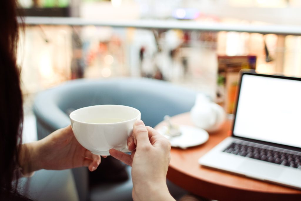 Gast met een kop koffie en een laptop in een horecagelegenheid