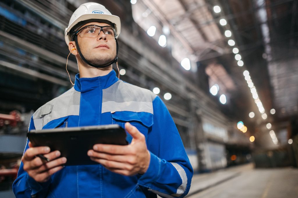 Medewerker met veiligheidshelm gebruikt een tablet in een fabriekshal