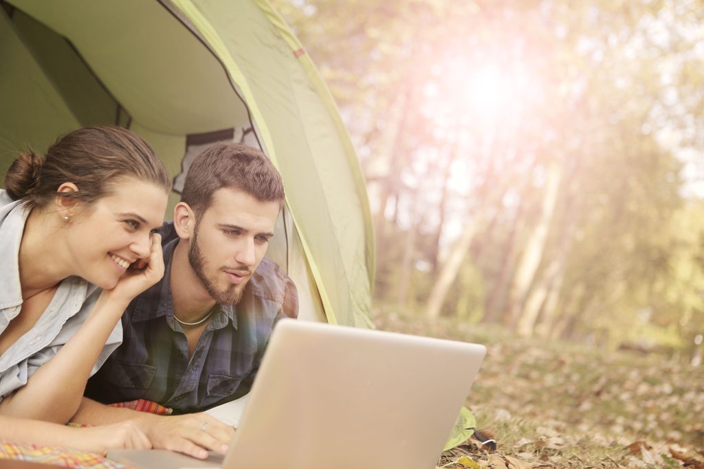 Twee kampeerders gebruiken samen een laptop bij hun tent